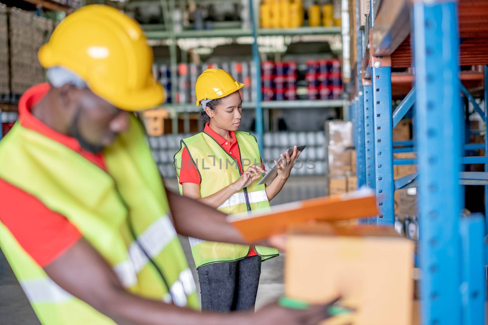 African American warehouse woman or factory worker check order or list of product using tablet and her co-worker stay in front of her in workplace area. Concept of good management of staff working.