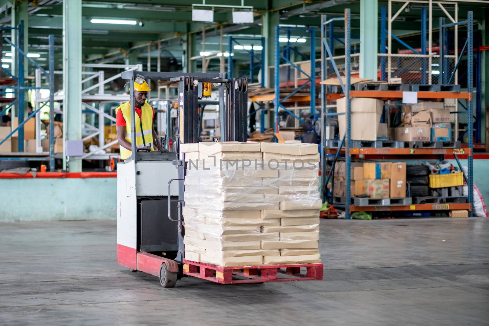 African American factory man or warehouse worker stand on forklift during work in workplace area to transfer pack of product. Concept of good management work in delivery industrial business.