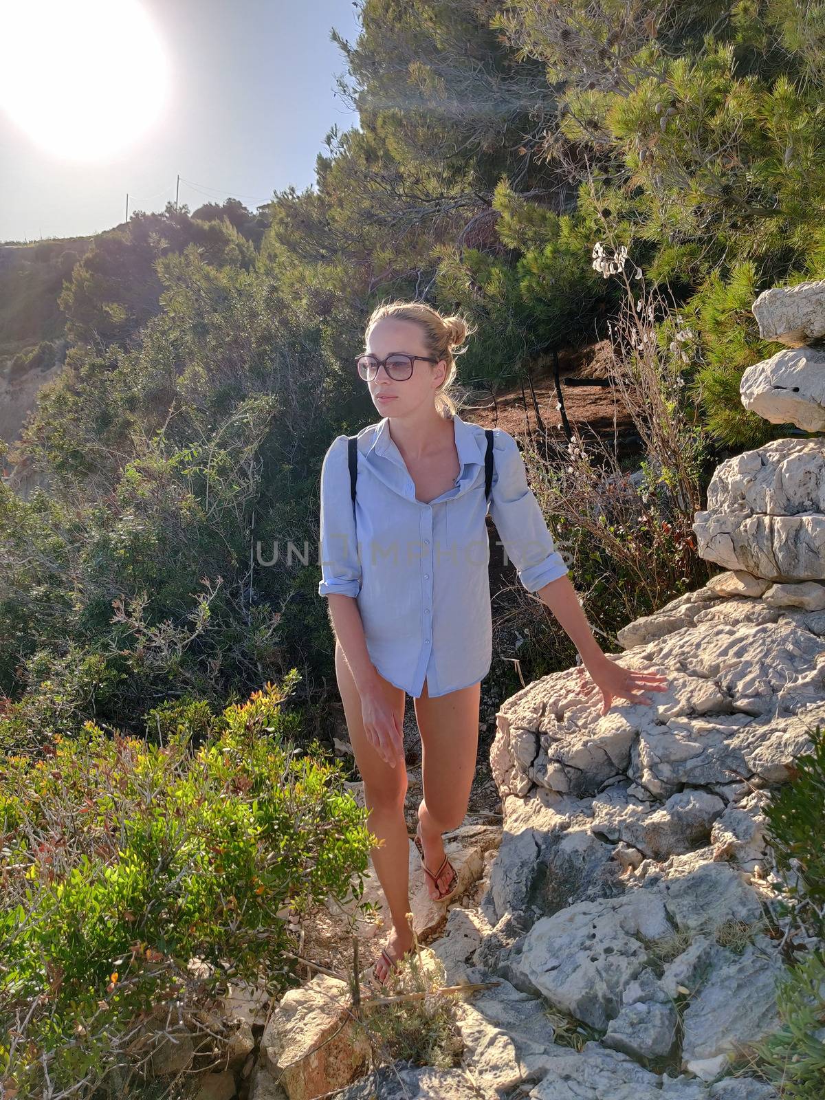 Young active feamle tourist wearing small backpack walking on coastal path among pine trees looking for remote cove to swim alone in peace on seaside in Croatia. Travel and adventure concept by kasto