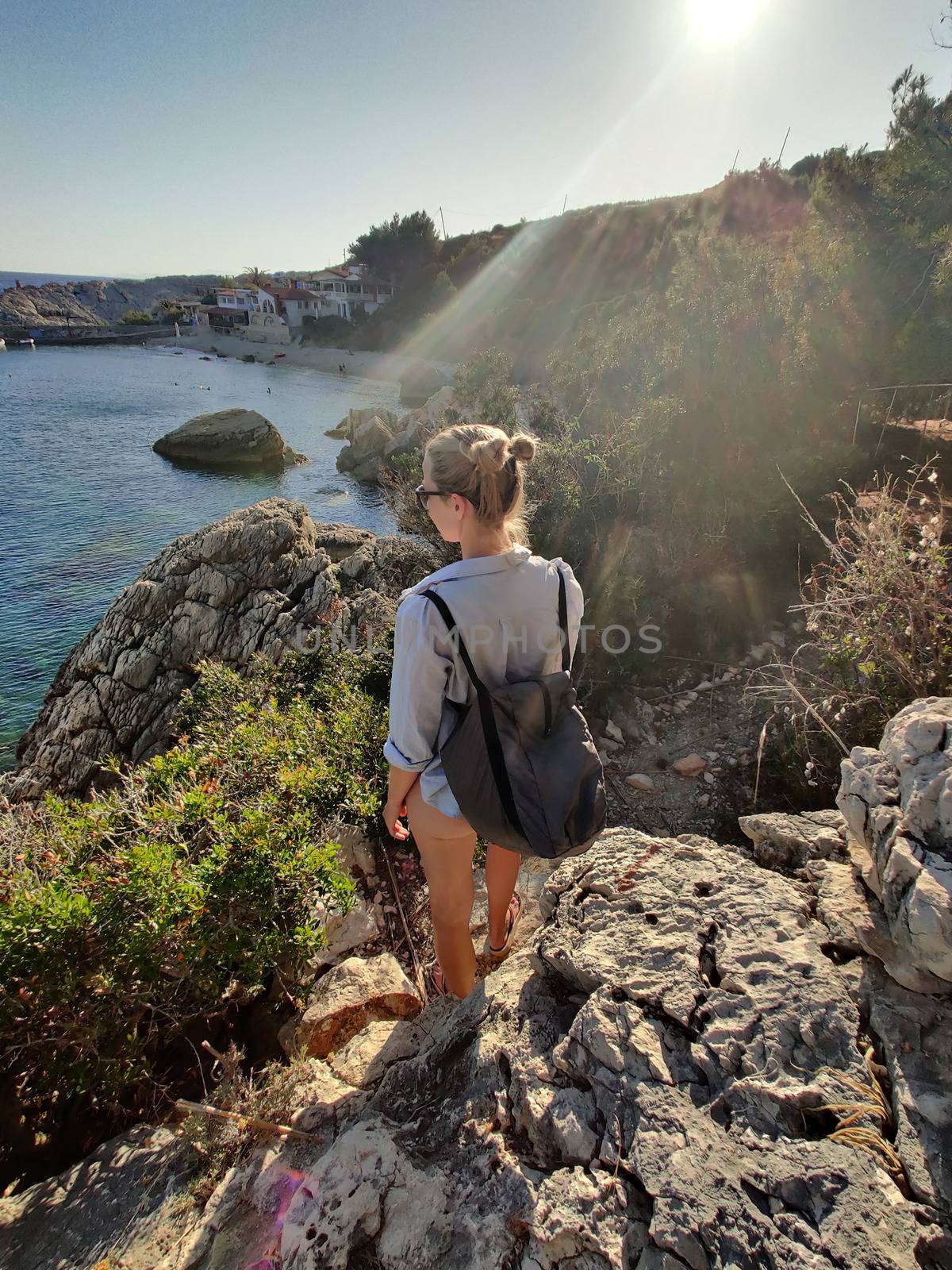 Young active feamle tourist wearing small backpack walking on coastal path among pine trees enjoing beautiful costal view of Velo Zarace beach on Hvar island, Croatia. Travel and adventure concept.