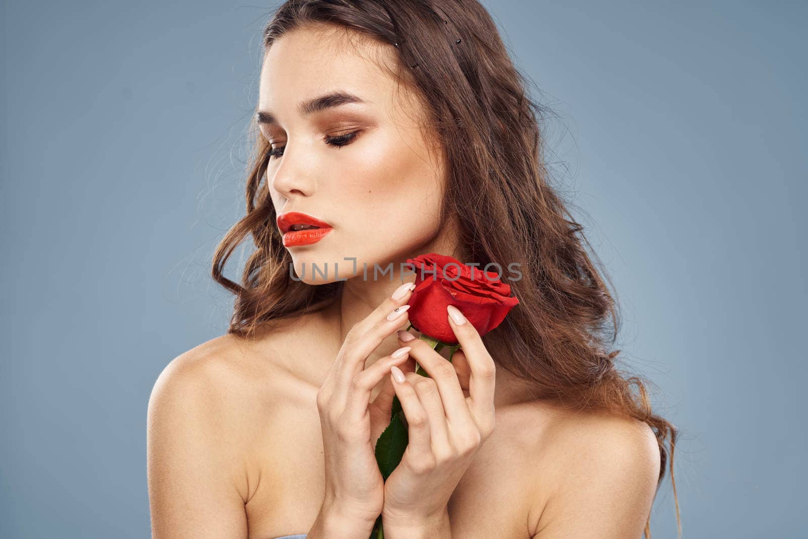 Woman portrait with red rose near the face on gray background and makeup curly hair. High quality photo