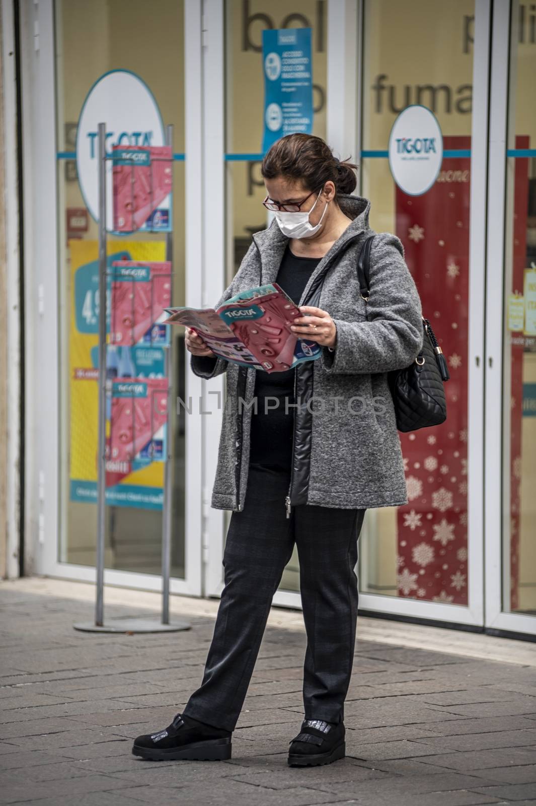 woman wearing medical mask in front of a shop looking at a brochure by carfedeph