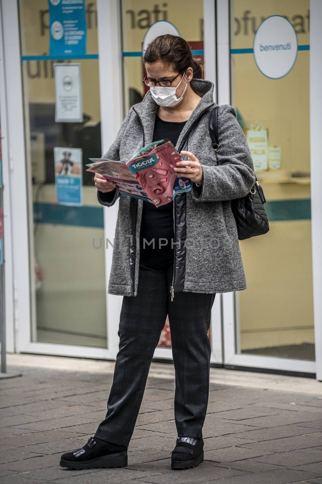 terni,itali november 05 2020:woman wearing medical mask in front of a shop looking at a brochure