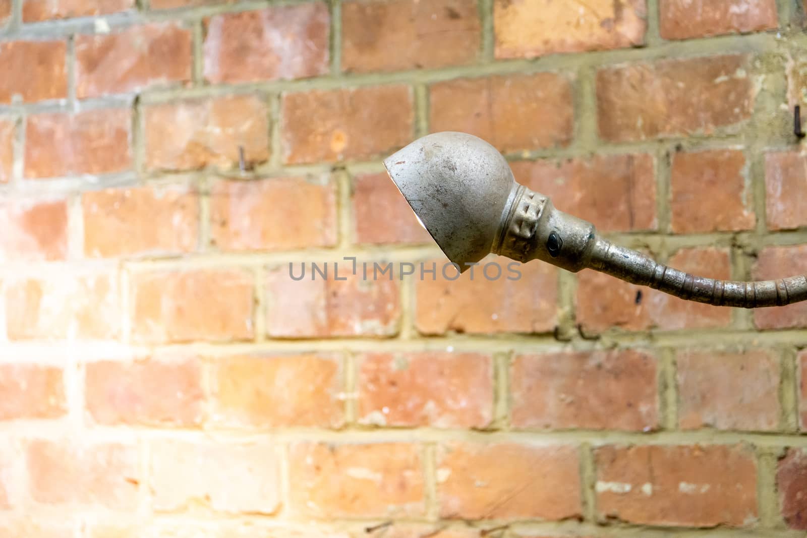 Old and rusty vintage industrial lamp shedding light on a red brick wall by kb79