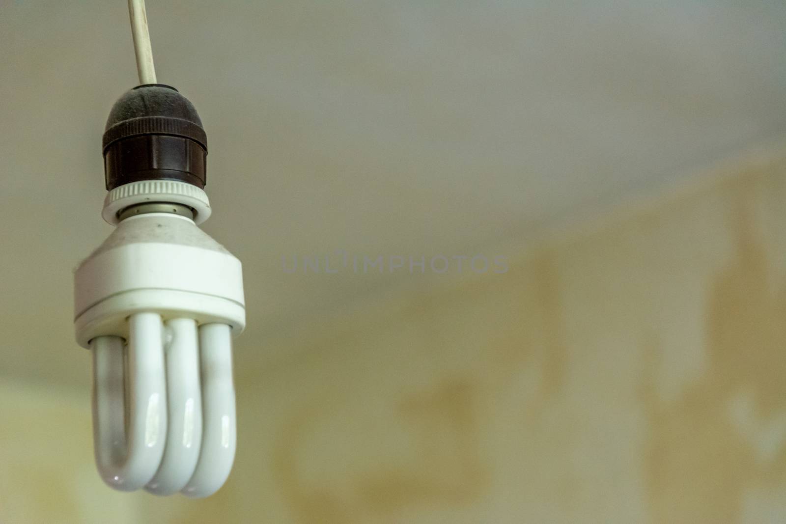Electrical CFL lamp on barebone socket in old an grunge style room indicating poverty and difficulties paying energy bills
