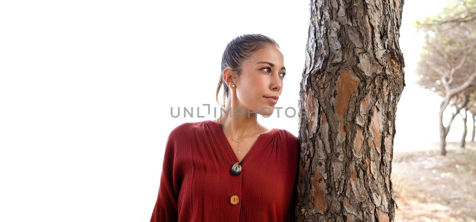 Half-length portrait of a beautiful young Caucasian woman with her hair gathered up that highlights the perfect features of the face - Close up of model posing near a tree with large white copy space by robbyfontanesi