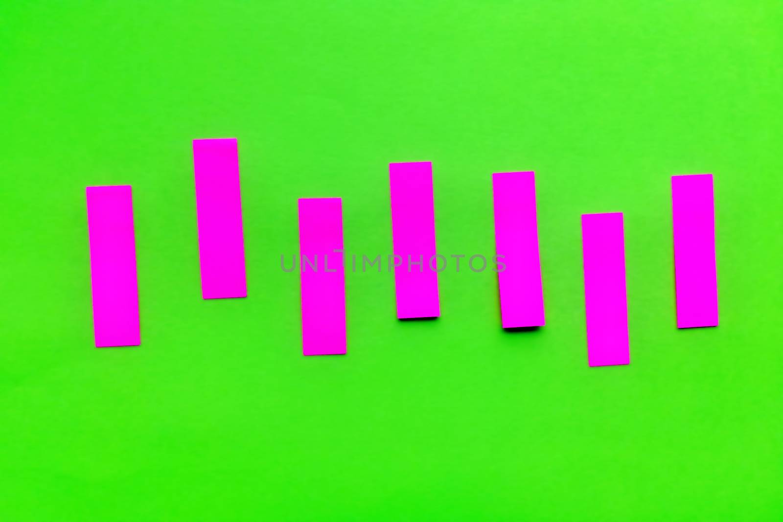 Purple pink vertical paper stickers on bright green paper. Horizontal shot. Front view.