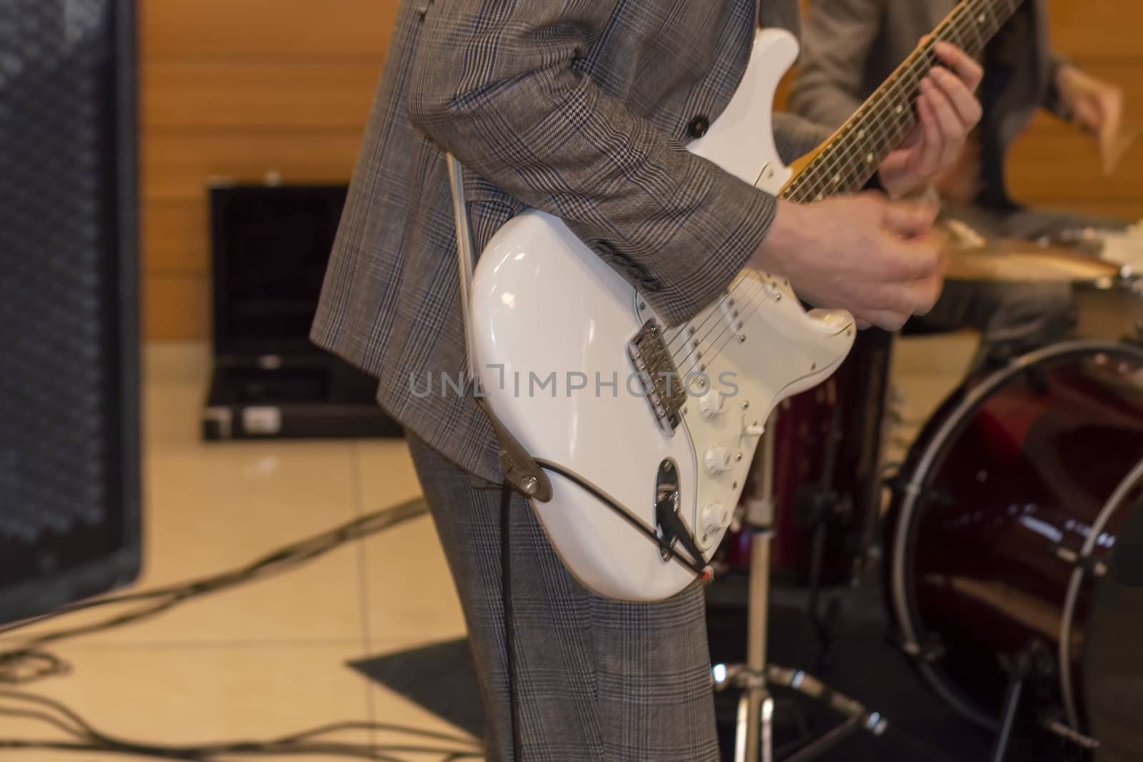 Grey suit and white guitar. There's a drum kit in the background.