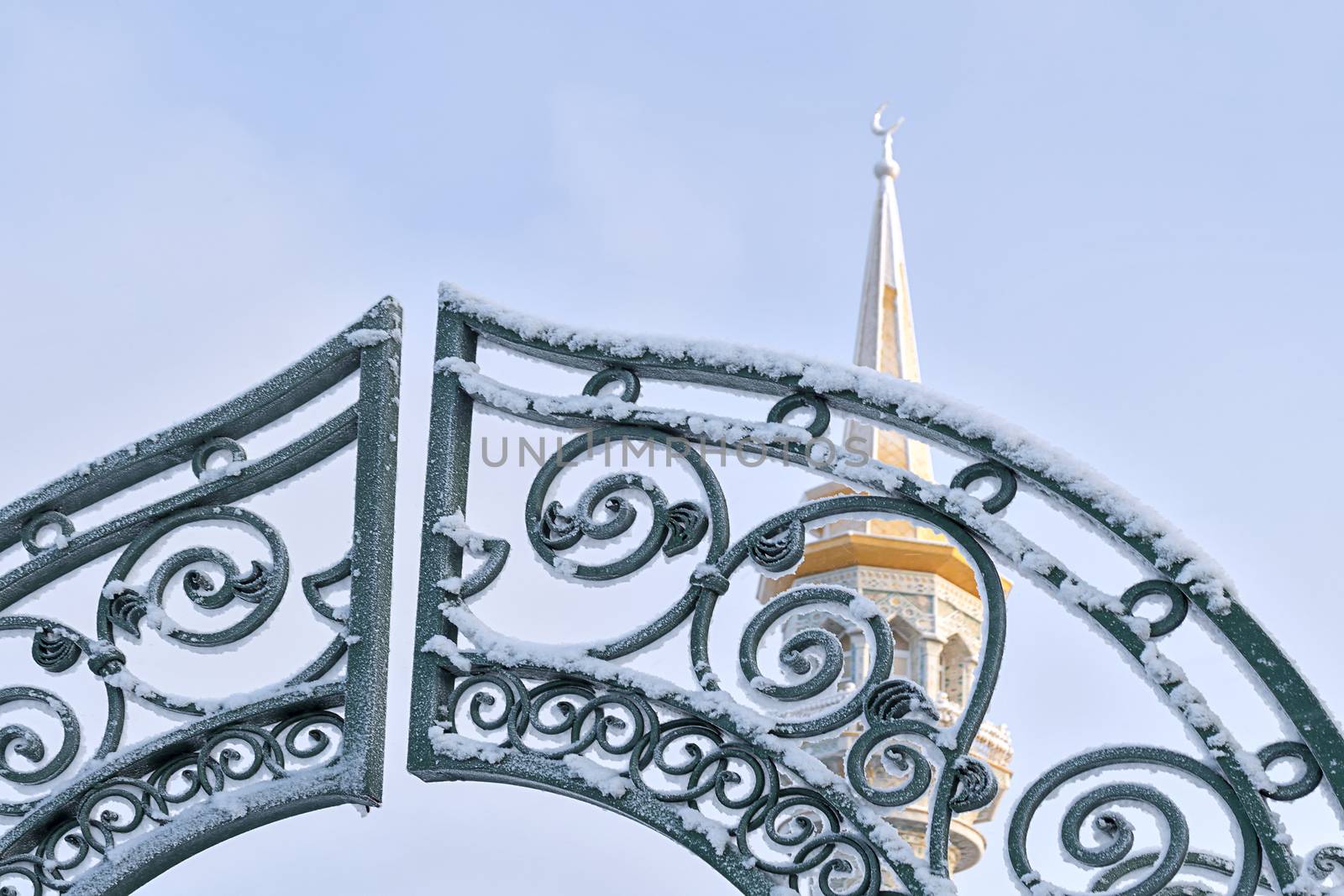 Gate to mosque and minaret in background against blue sky in winter. View from below.