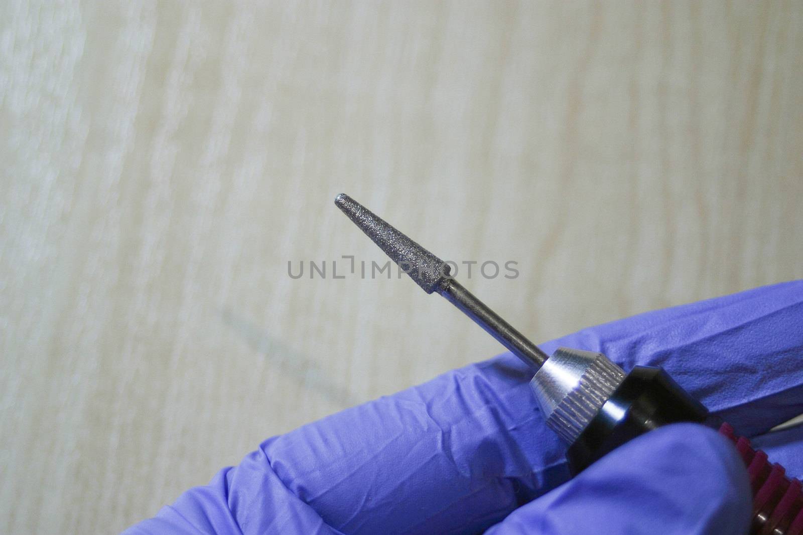 Milling cutter in a manicurist hand on a wood background. Manicure and pedicure professional tools.