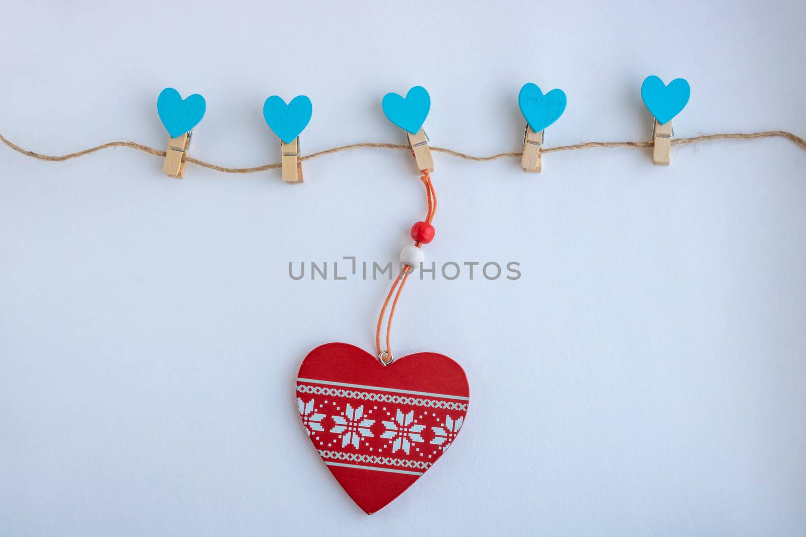A red wooden heart hangs on a clothespin with a rope on a white background. The concept of Valentine's day, mother's day, 8 March.