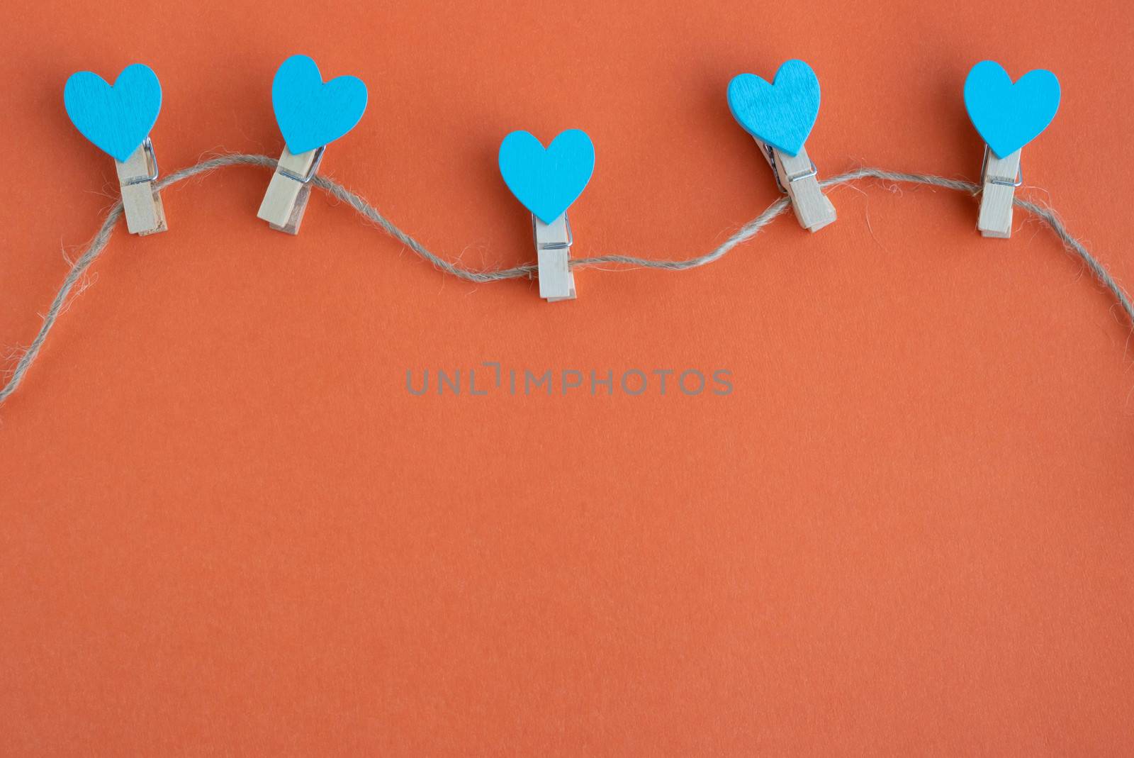 Small clothespins and blue hearts on a rope on an orange background