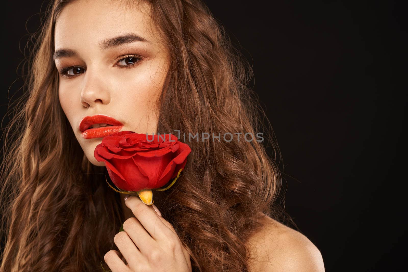 woman with a red rose on a dark background long hair makeup red lips. High quality photo