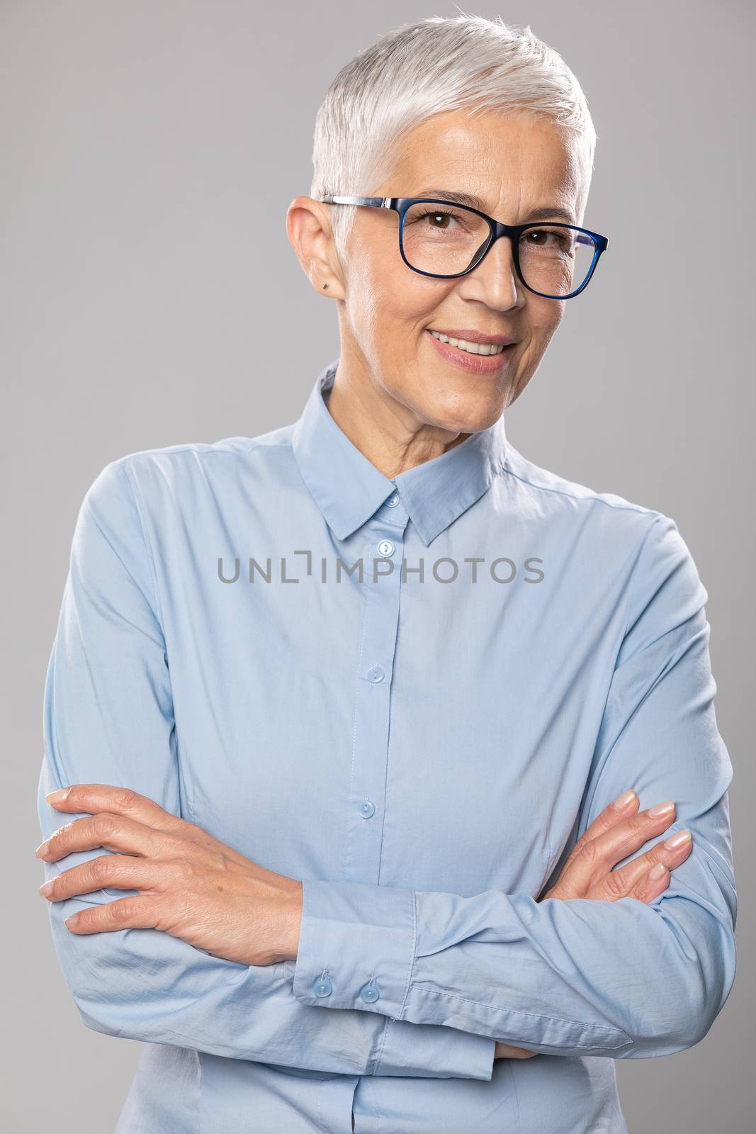 Senior businesswoman with glasses in a blue shirt and gray white by adamr