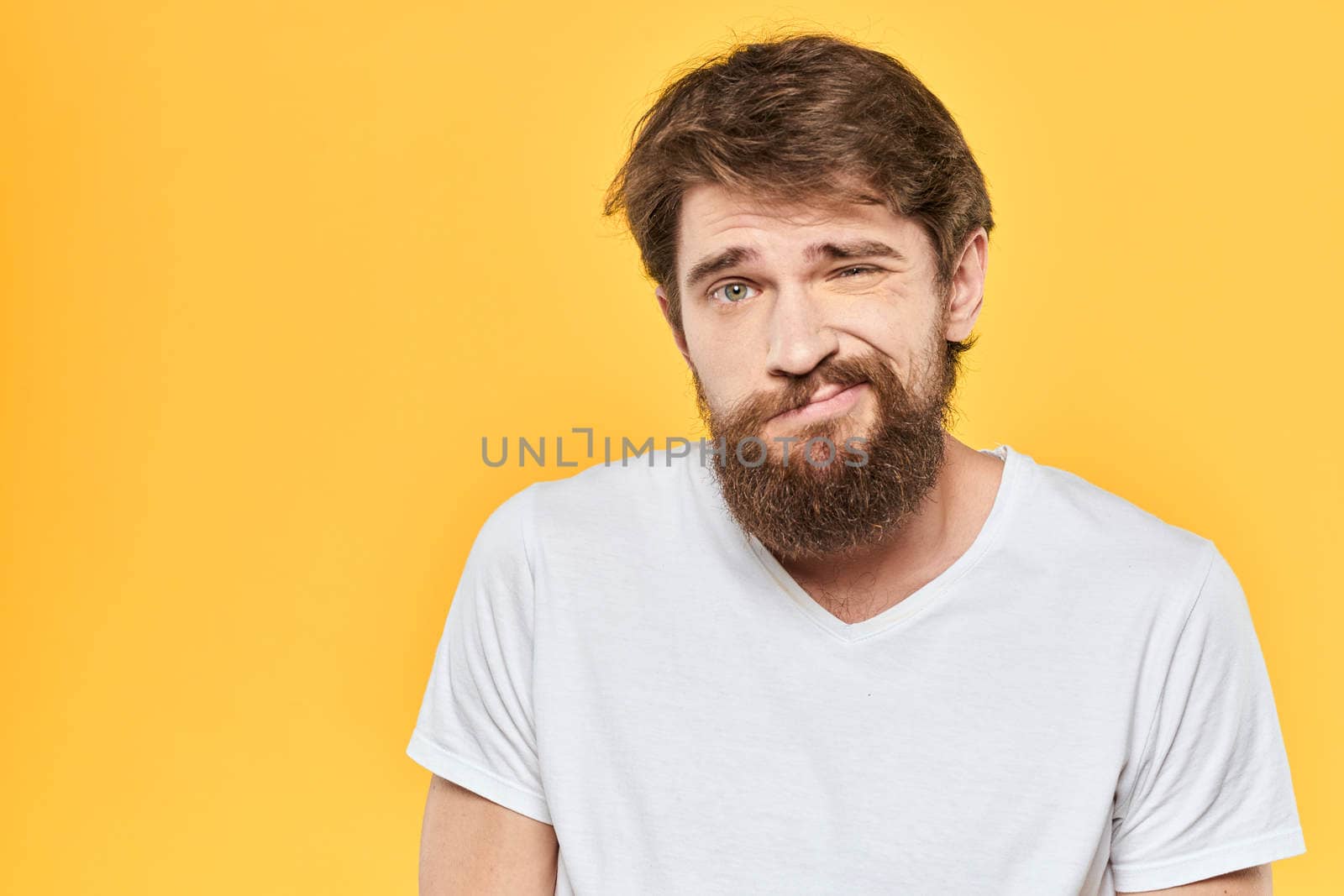 Bearded man in a white T-shirt gestures with his hands emotions studio yellow background by SHOTPRIME