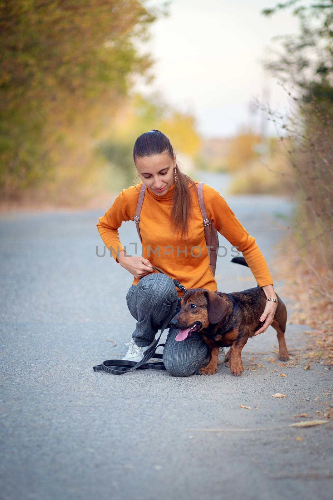 Young woman in orange turtleneck and jeans walks and hugs the dog
