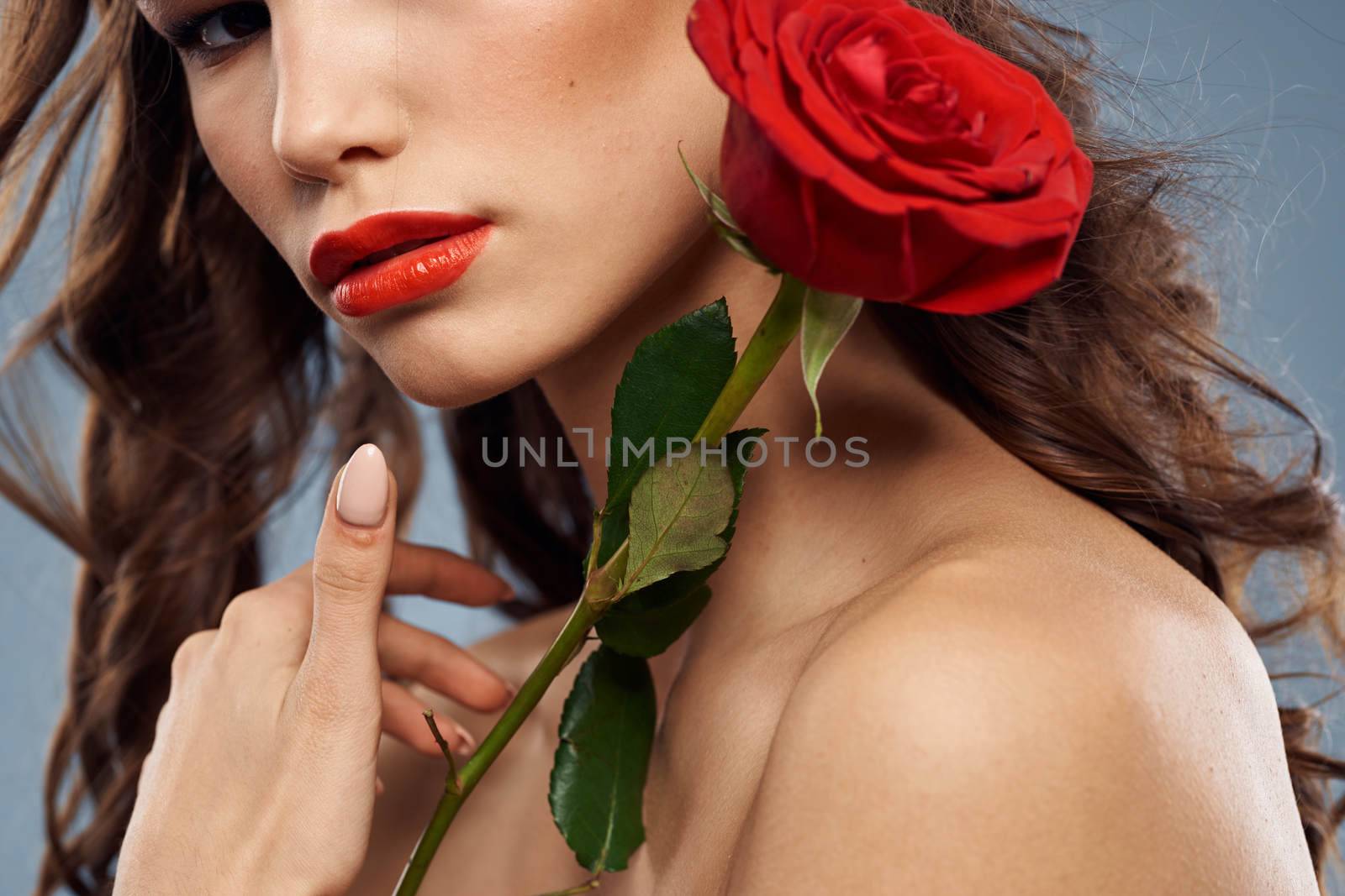 Portrait of a woman with a red rose in her hands on a gray background naked shoulders evening makeup. High quality photo