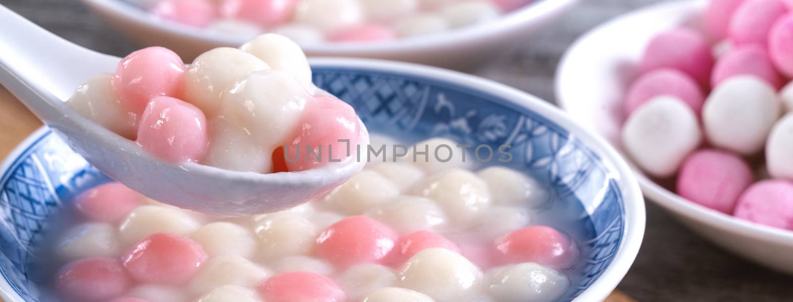 Close up of red and white tangyuan (tang yuan, glutinous rice dumpling balls) in blue bowl on wooden background for Winter solstice festival food.