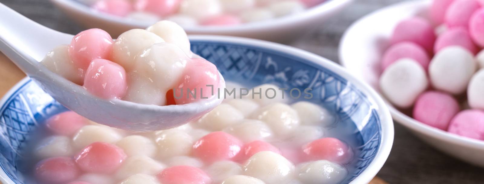 Close up of red and white tangyuan in blue bowl on wooden backgr by ROMIXIMAGE