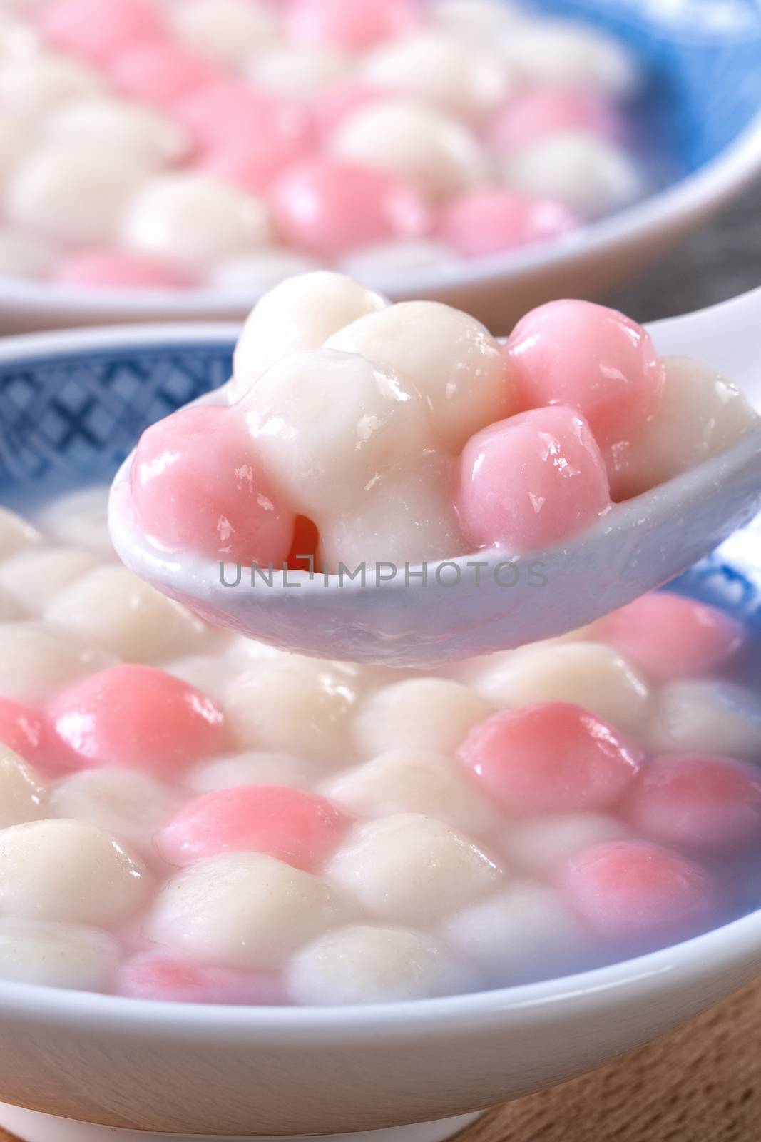 Close up of red and white tangyuan (tang yuan, glutinous rice dumpling balls) in blue bowl on wooden background for Winter solstice festival food.