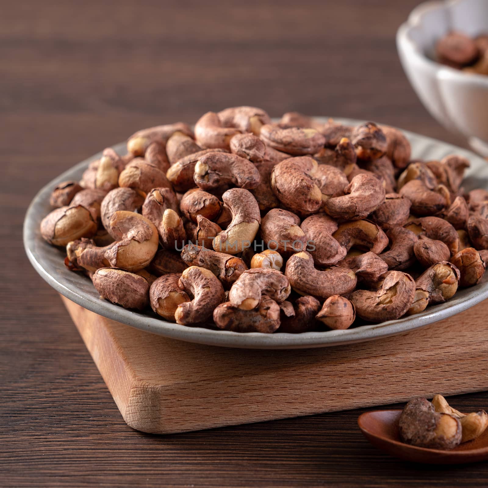 Cashew nuts with peel in a plate on wooden tray and table background, healthy raw food concept.