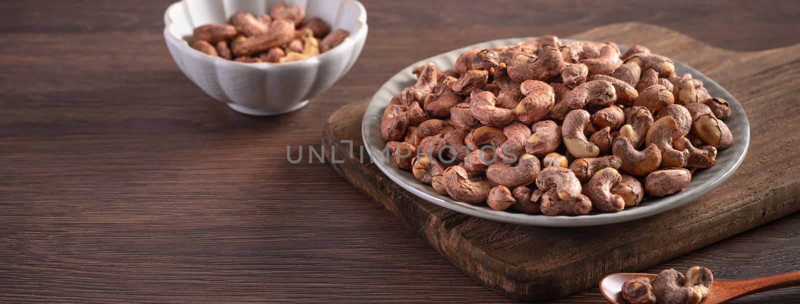 Cashew nuts with peel in a plate on wooden tray and table background, healthy raw food concept.