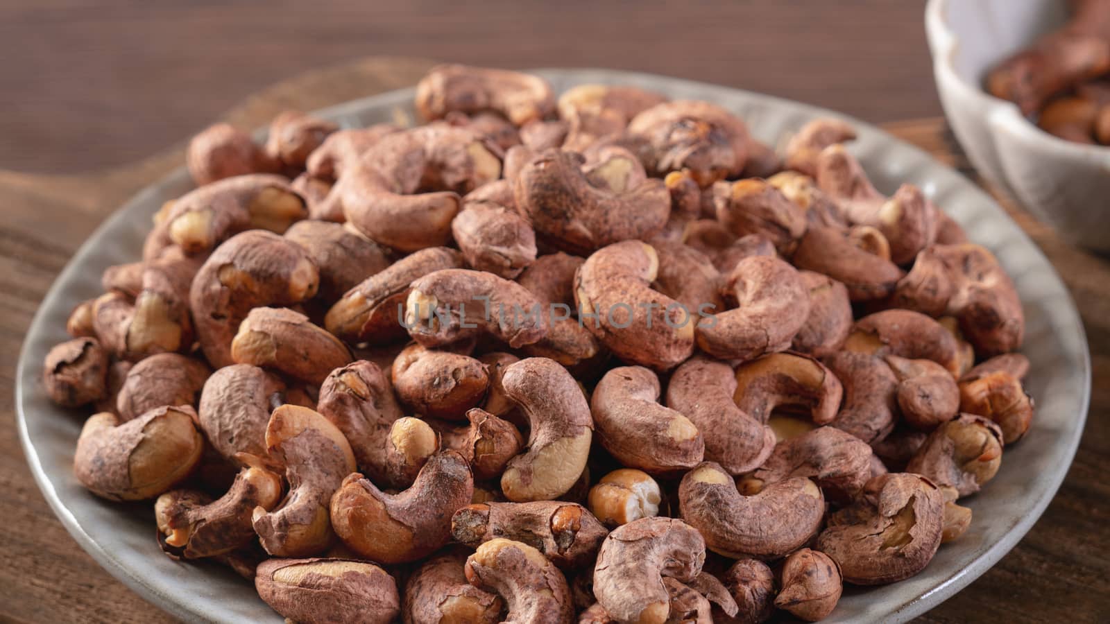 Cashew nuts with peel in a plate on wooden tray and table background, healthy raw food concept.