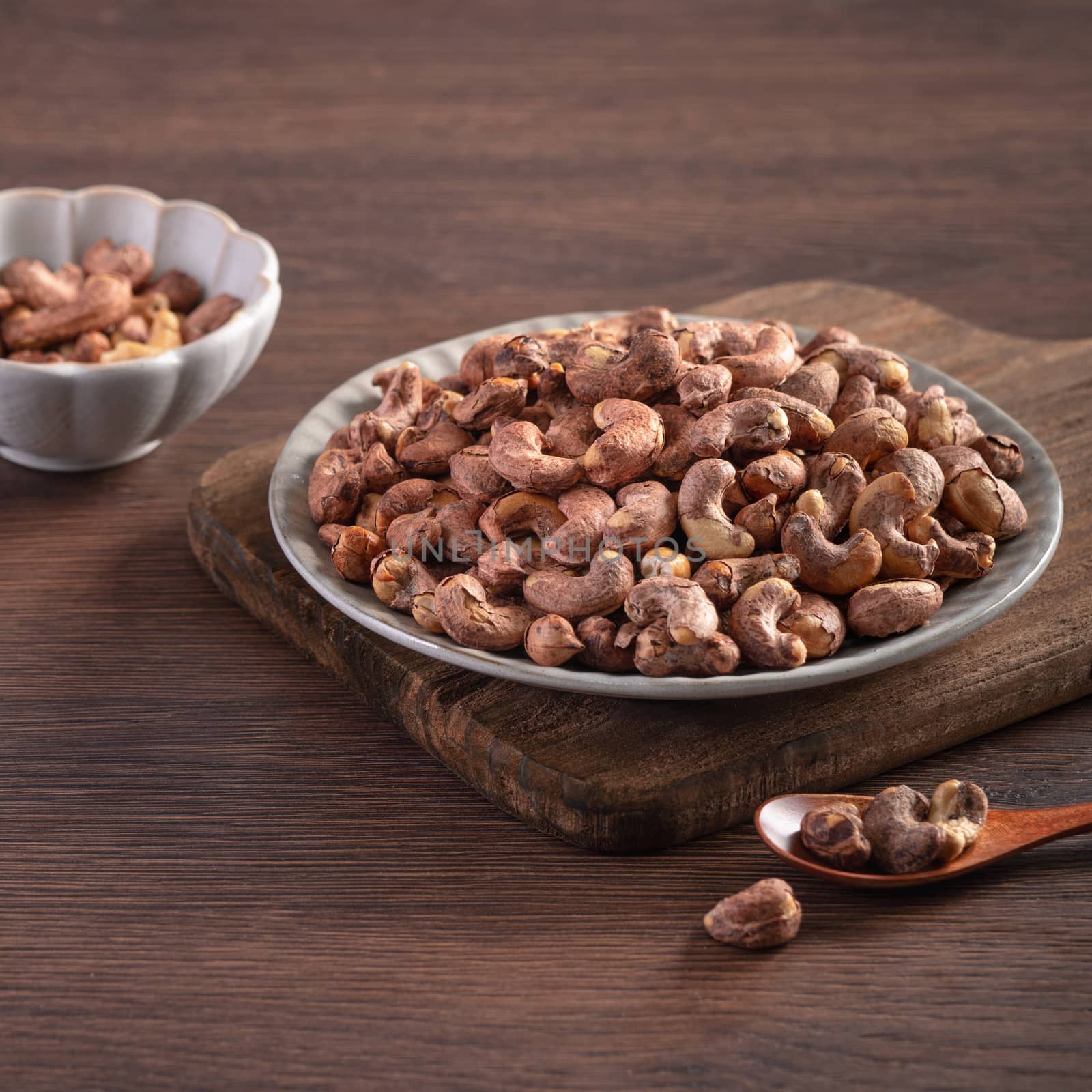 Cashew nuts with peel in a plate on wooden tray and table background, healthy raw food concept.