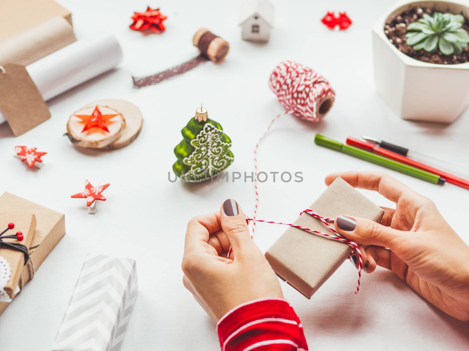 White table with Christmas decorations. Woman wraps New Year gift on craft paper. Winter holiday spirit.