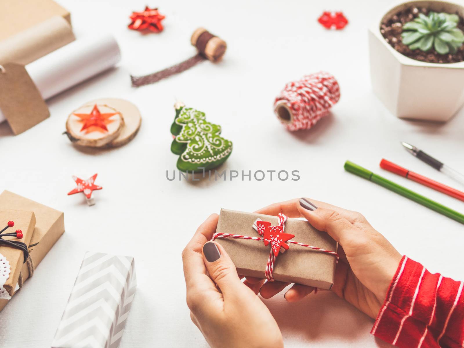 White table with Christmas decorations. Woman wraps New Year gift on craft paper. Winter holiday spirit.