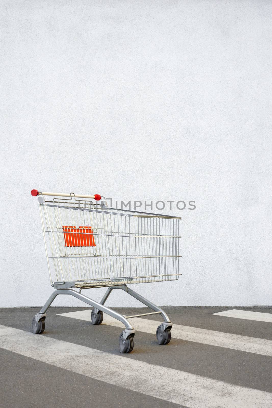Empty Shopping Cart Trolley Stands near Mall with Copy Space. Grocery Cart on the White Wall Store. Trolley at the Supermarket Background. E-commerce. Shopping Concept. Side View. Shopping Service by synel