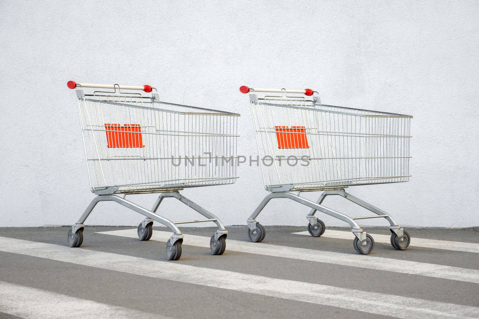 Two Empty Shopping Cart Trolley Stands near Mall with Copy Space. Grocery Cart on the White Wall Store. Trolley at the Supermarket Background. E-commerce. Shopping Concept. Side View. Shopping Service