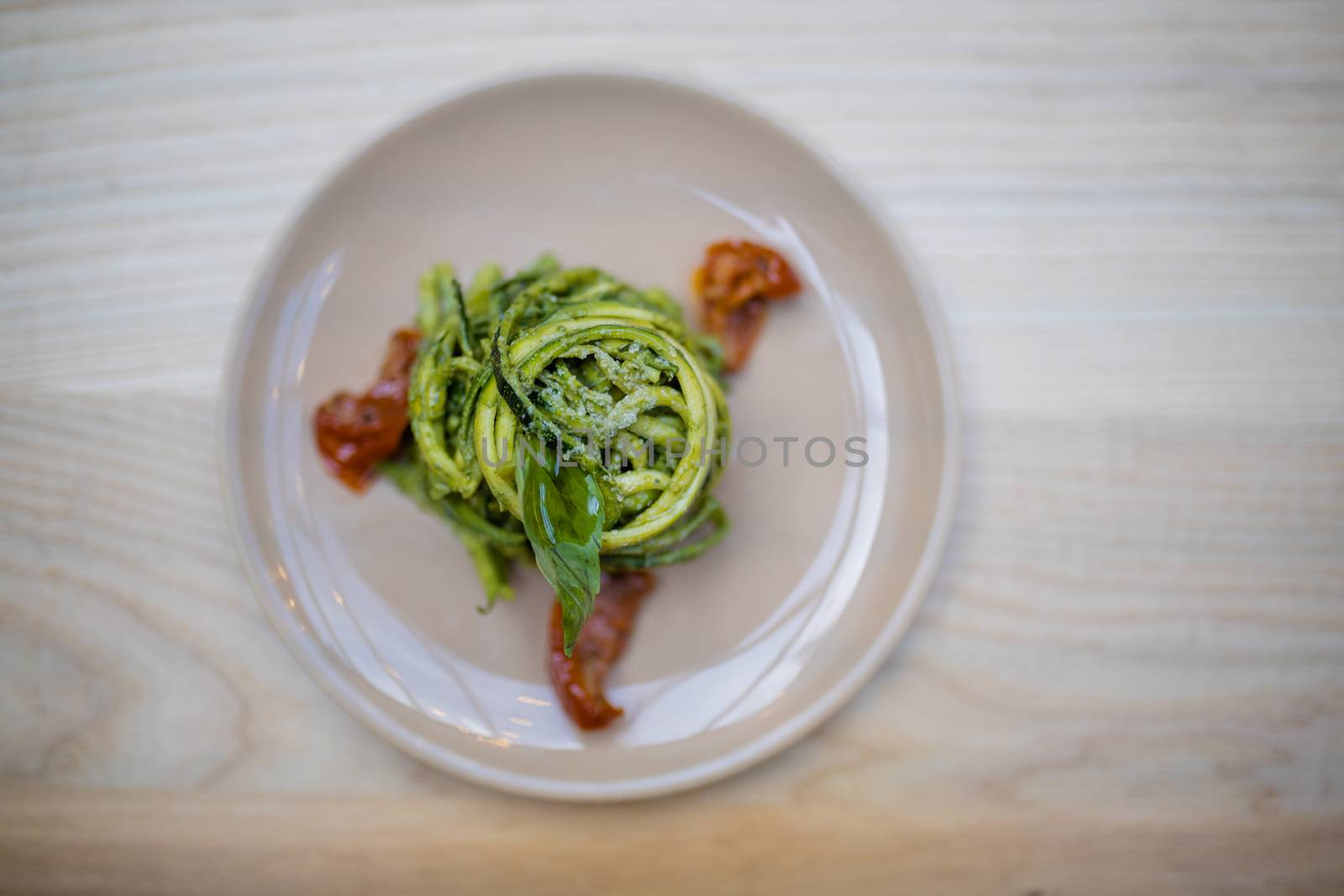 Above view of tasty looking zucchini noodles with a spinach leaf on top and on a wooden restaurant table