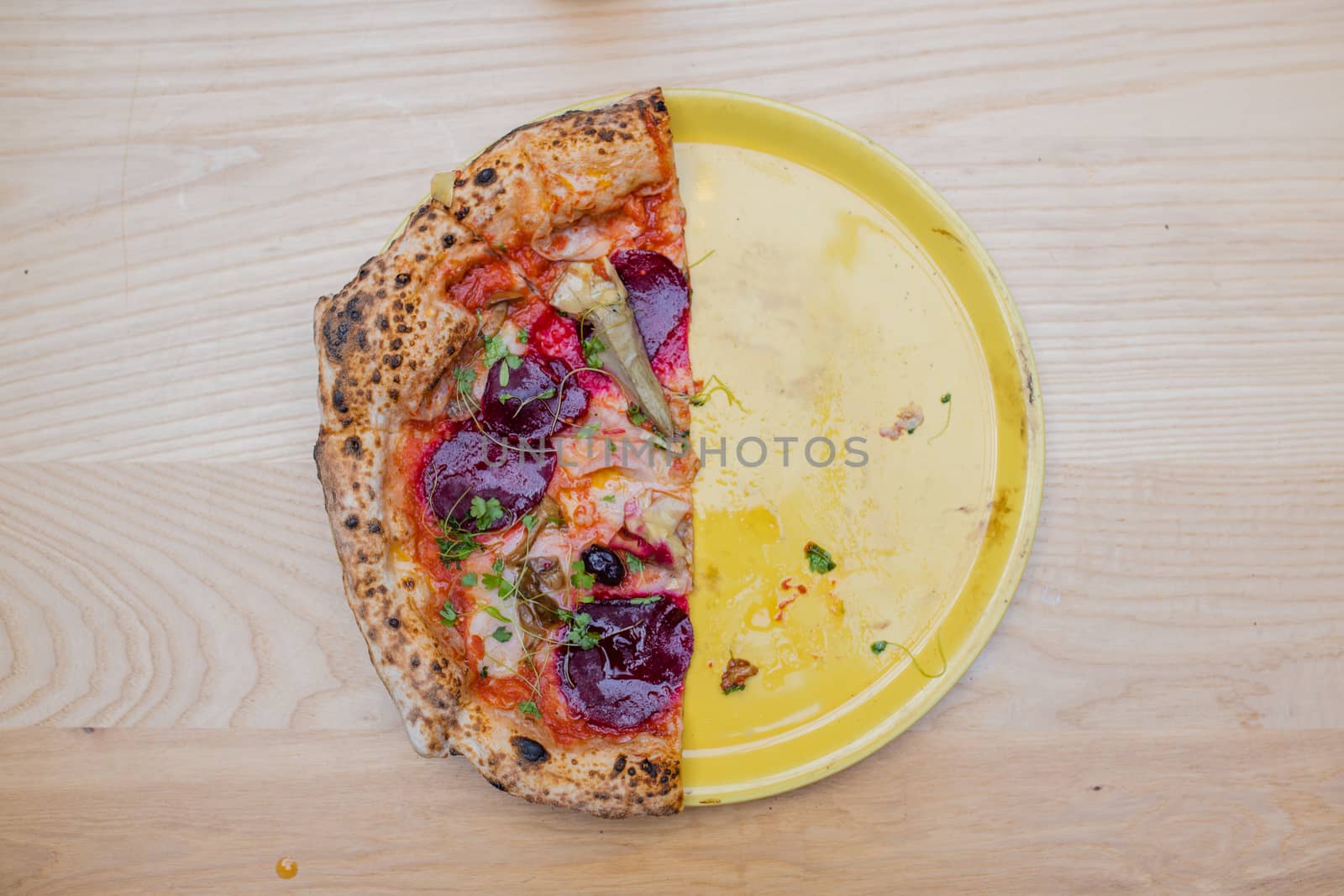 Above view of half a thick and tasty looking vegan pizza on a yellow plate above a wooden table