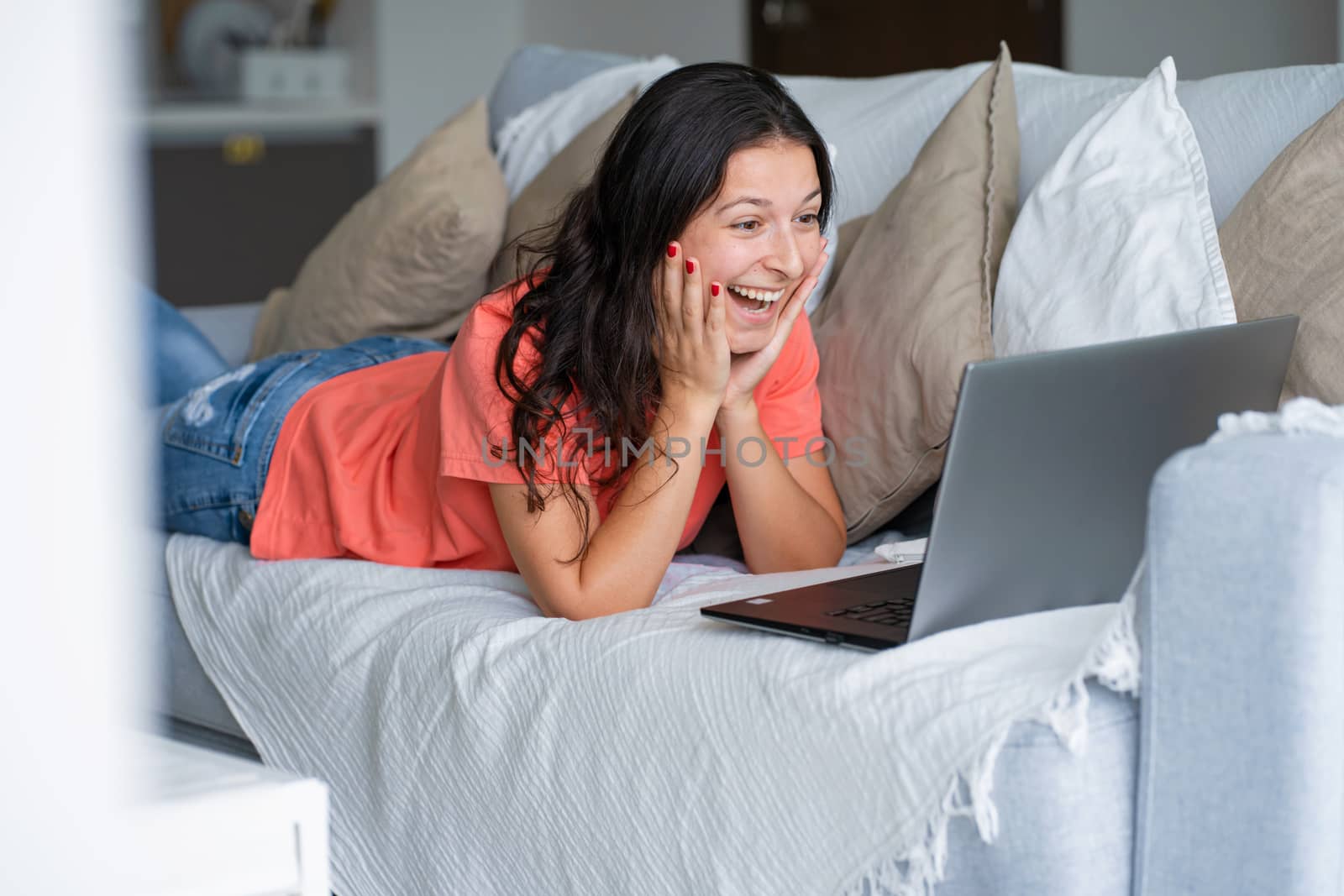 Girl lying on the couch rejoices looking at the laptop. Smiles, good mood, emotion of joy.
