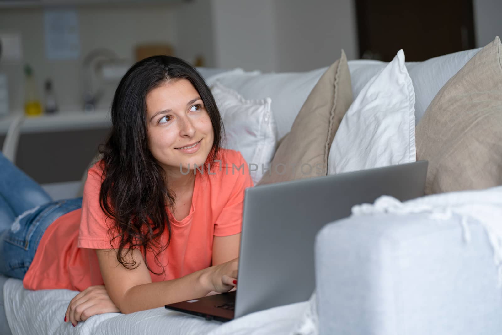 Girl lying on the couch rejoices looking at the laptop. Smiles, good mood, emotion of joy.