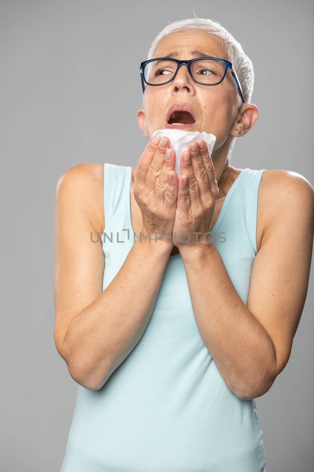 Senior women with short gray hair coughs and sneezes into a handkerchief, studio shoot, allergies and illness concept