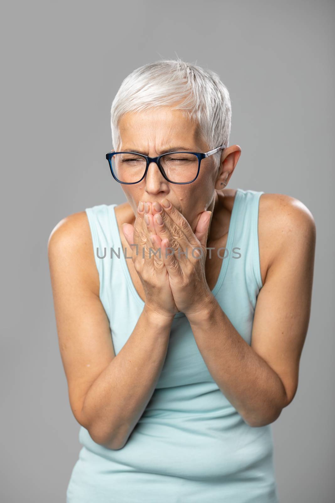 Senior women with glasses and short gray hair coughs and sneezes into a handkerchief, studio shoot, allergies and illness concept