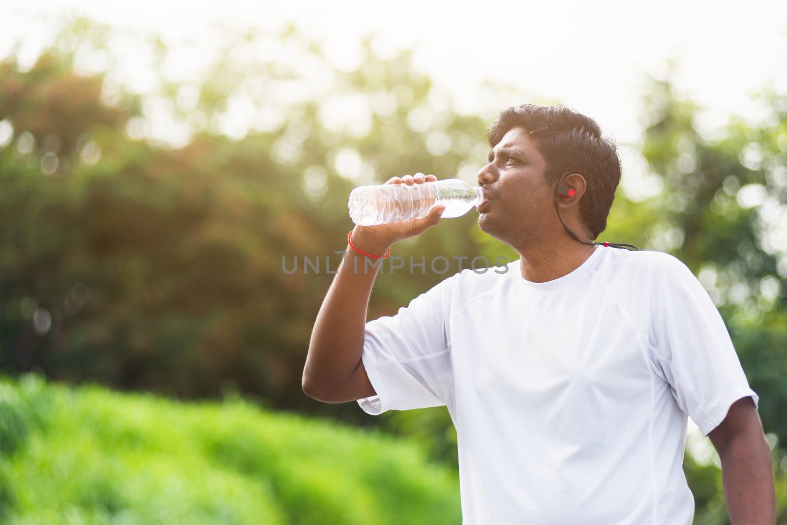 Close up Asian young sport runner black man wear athlete headphones he drinking water from a bottle after running at the outdoor street health park, healthy exercise workout concept