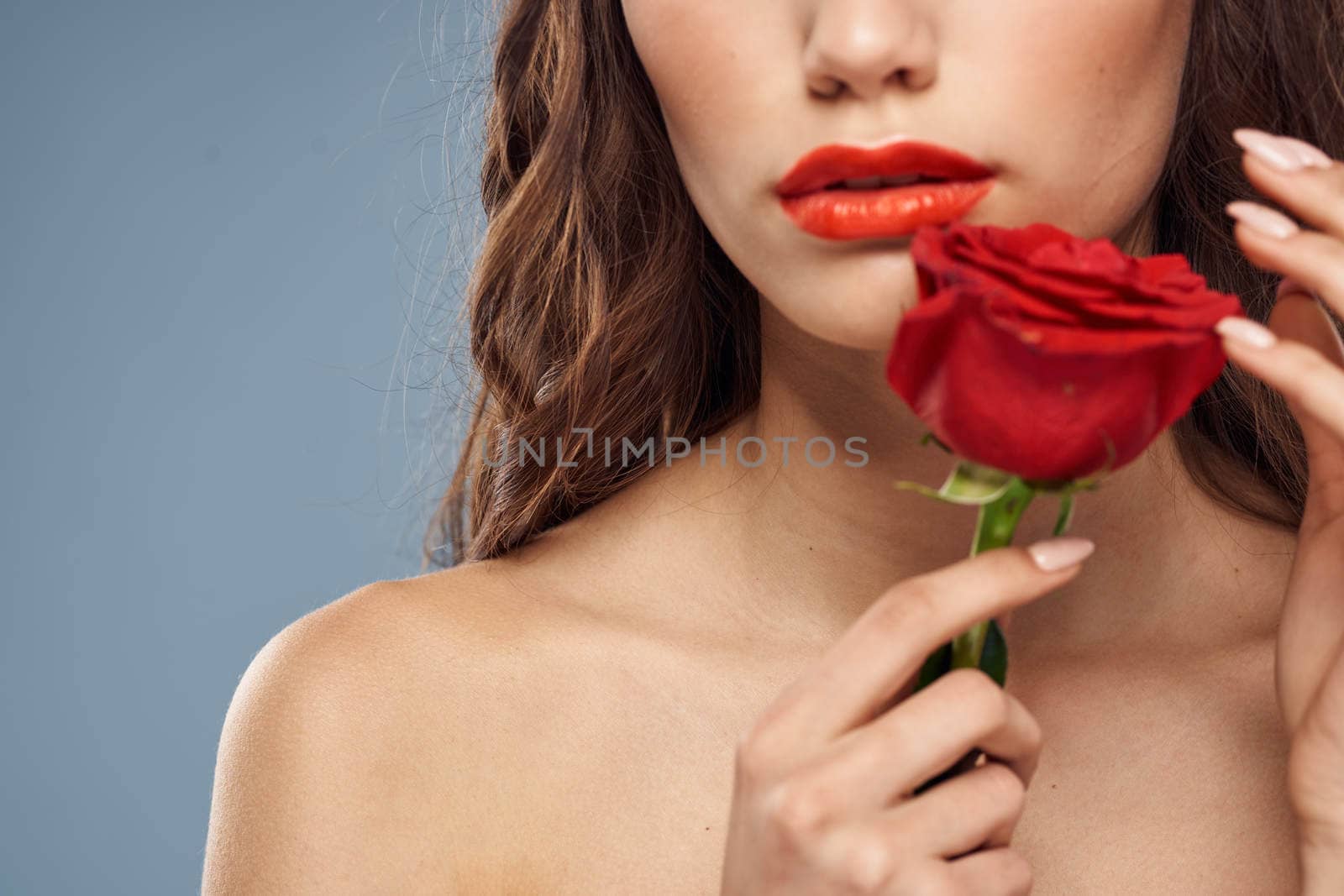 Woman portrait with red rose near the face on gray background and makeup curly hair. High quality photo