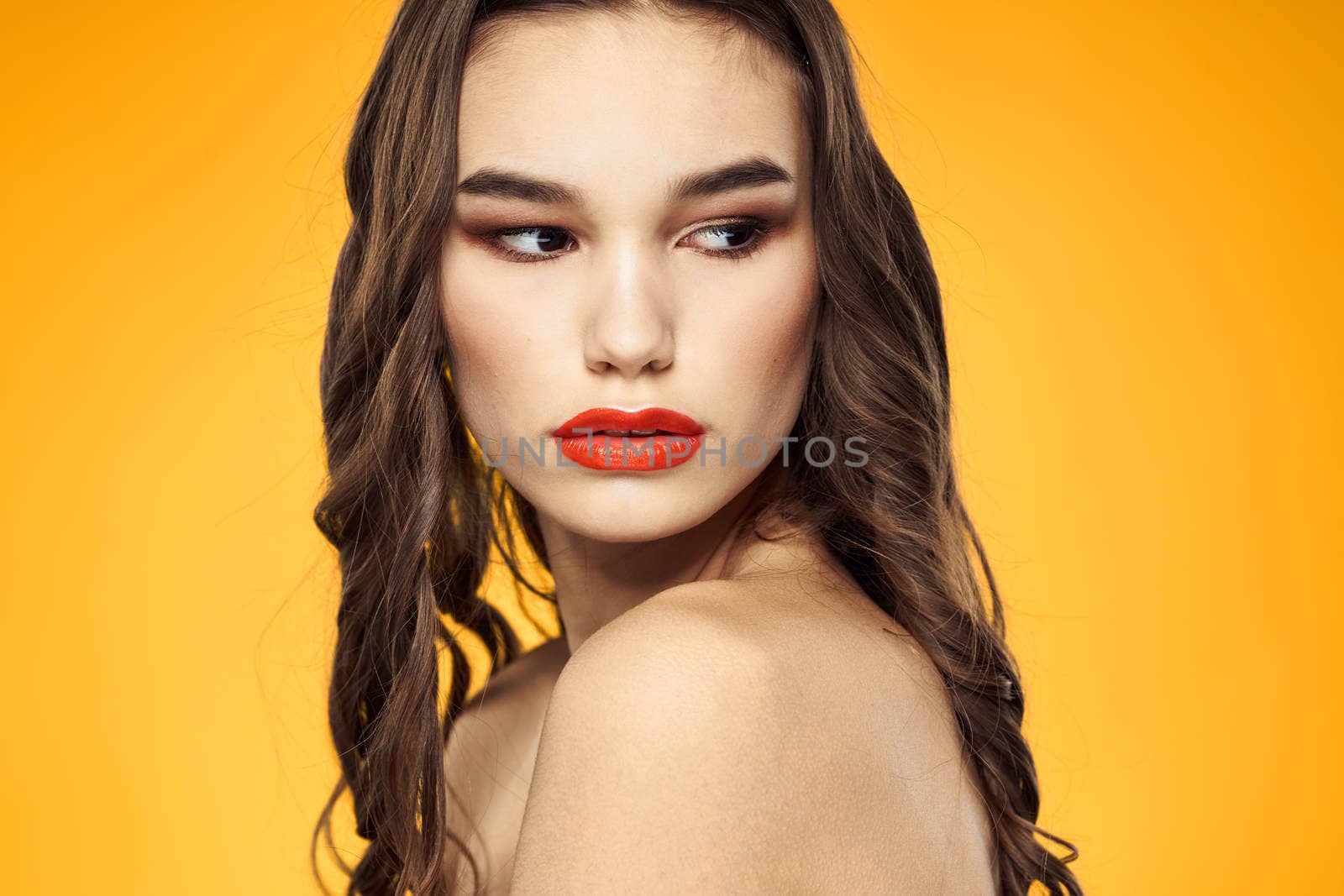 beautiful brunette red lips bare shoulders skin care yellow background. High quality photo