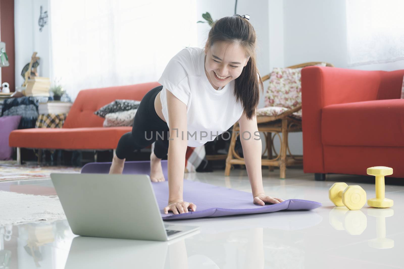 Fit woman doing yoga plank and watching online tutorials, training in living room. Stay at home life style.