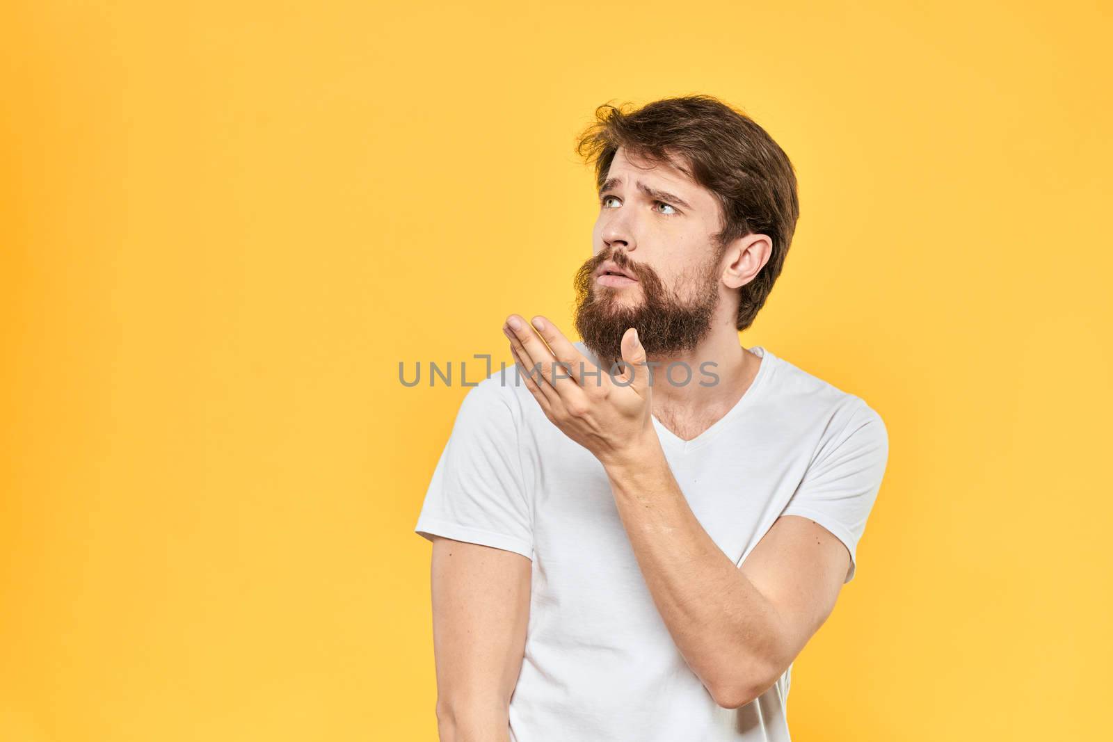 Bearded man emotions gestures with hands facial expression white t-shirt yellow background. High quality photo