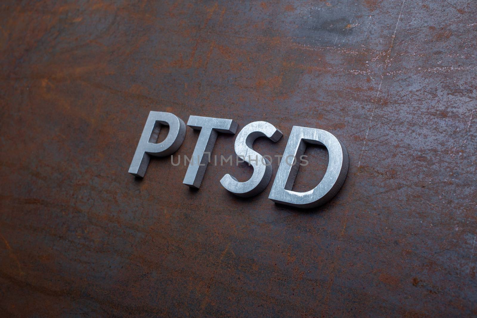the word PTSD - post traumatic stress disorder - laid with silver metal letters on flat rusted sheet steel background in slanted diagonal perspective.