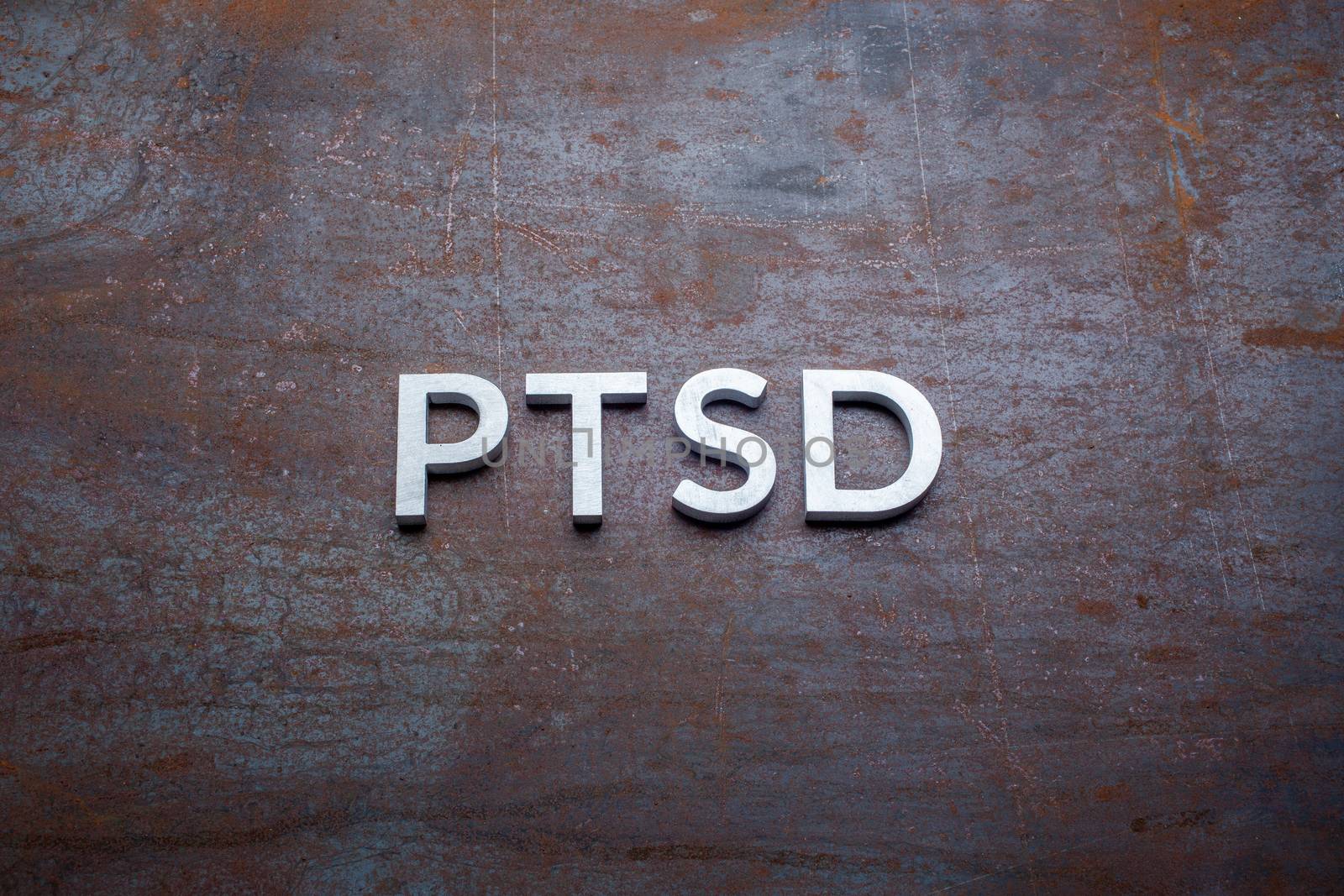 the word PTSD - post traumatic stress disorder - laid with silver metal letters on flat rusted sheet steel background in straight perspective.