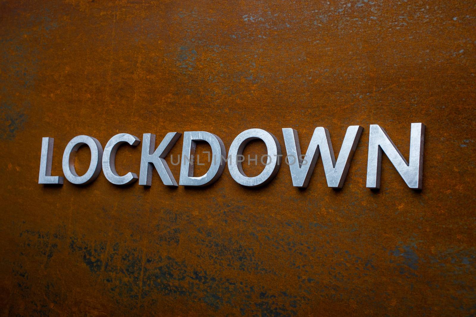 the word lockdown laid with silver metal letters on flat rusted steel sheet background in slanted linear perspective by z1b
