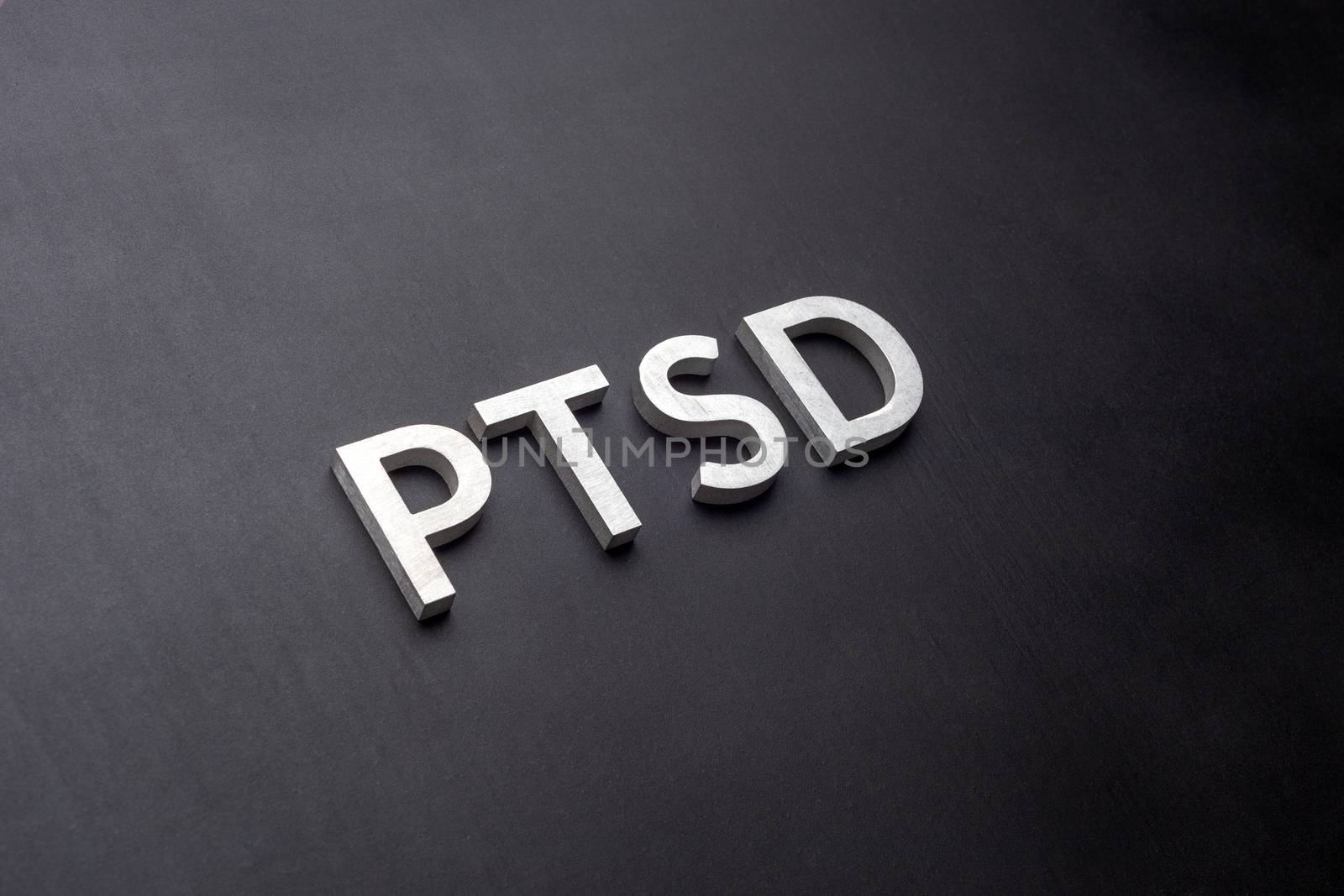 the word PTSD - post traumatic stress disorder - laid with silver metal letters on flat black background in linear perspective with selective focus