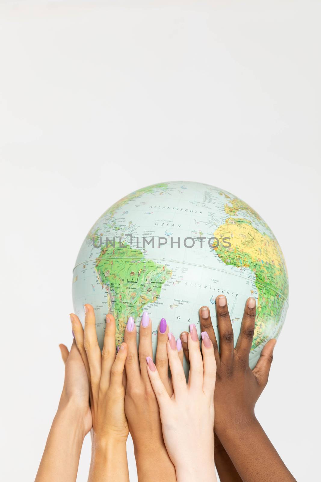 Four young adult girls hold the globe above their heads and gently embrace it with their hands. Colored hands of different races. by fotodrobik