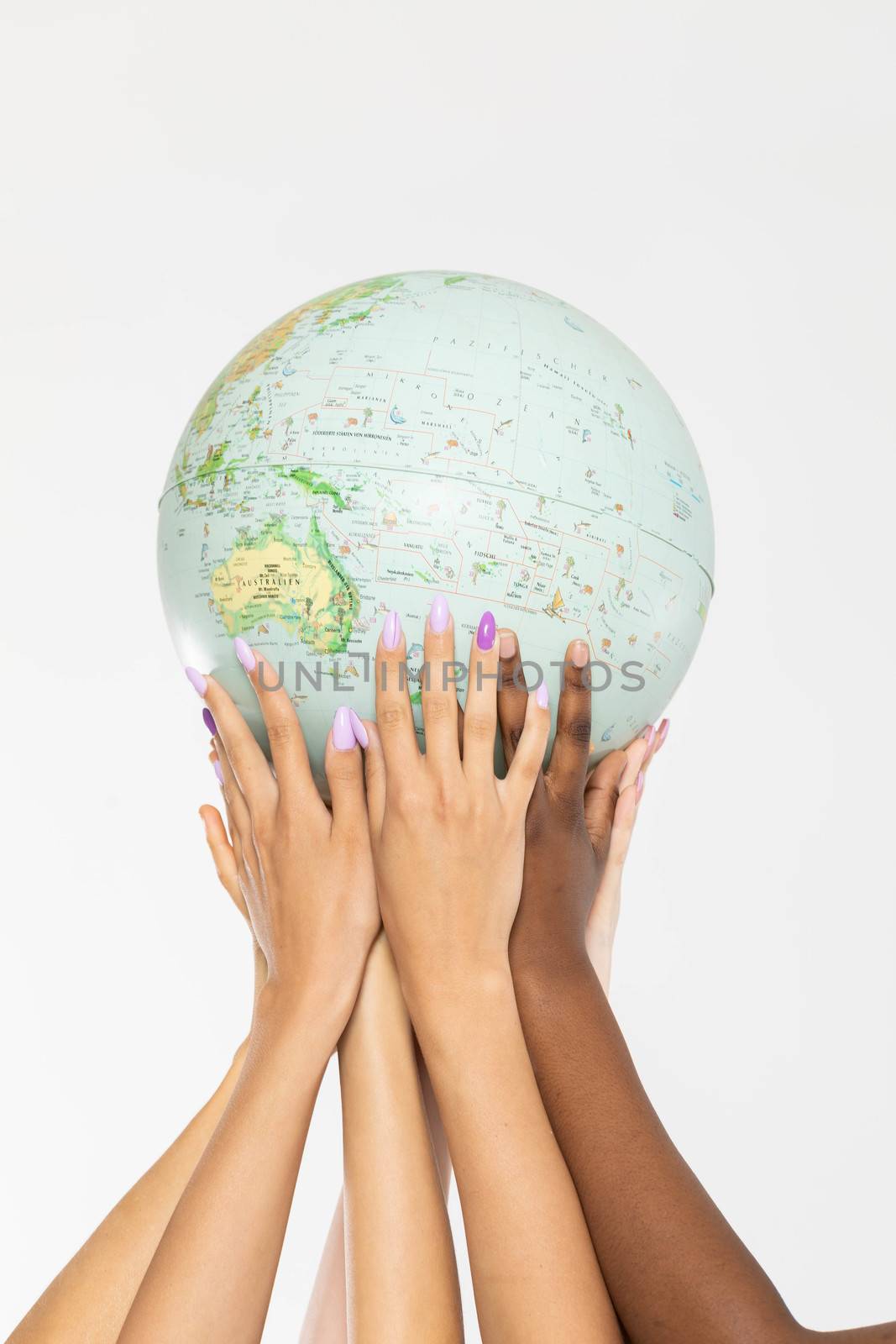 A large globe with all continents is supported by female hands of various races, symbolizing unity, acceptance and racial tolerance.