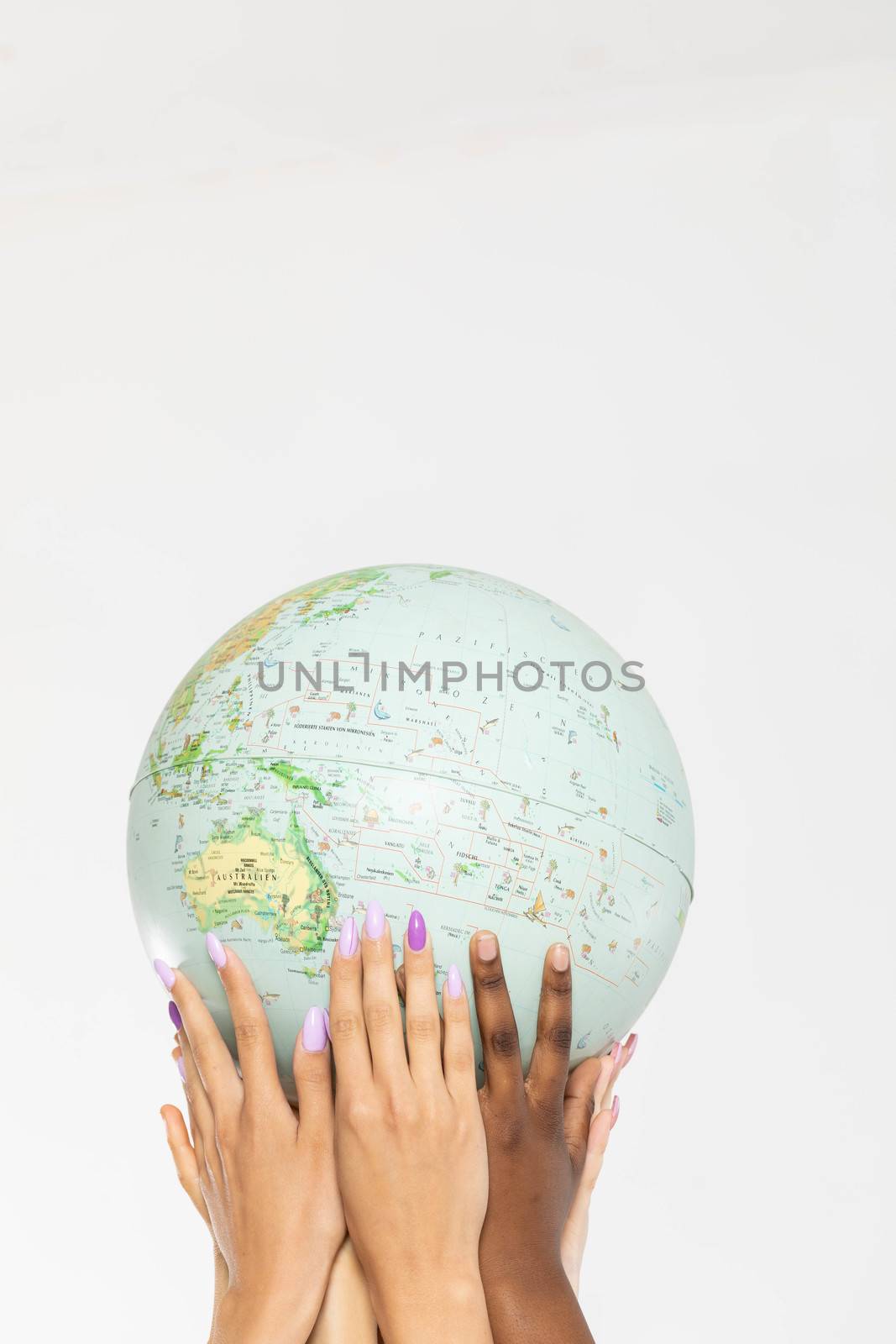 Four young adult girls hold the globe above their heads and gently embrace it with their hands. Colored hands of different races. by fotodrobik